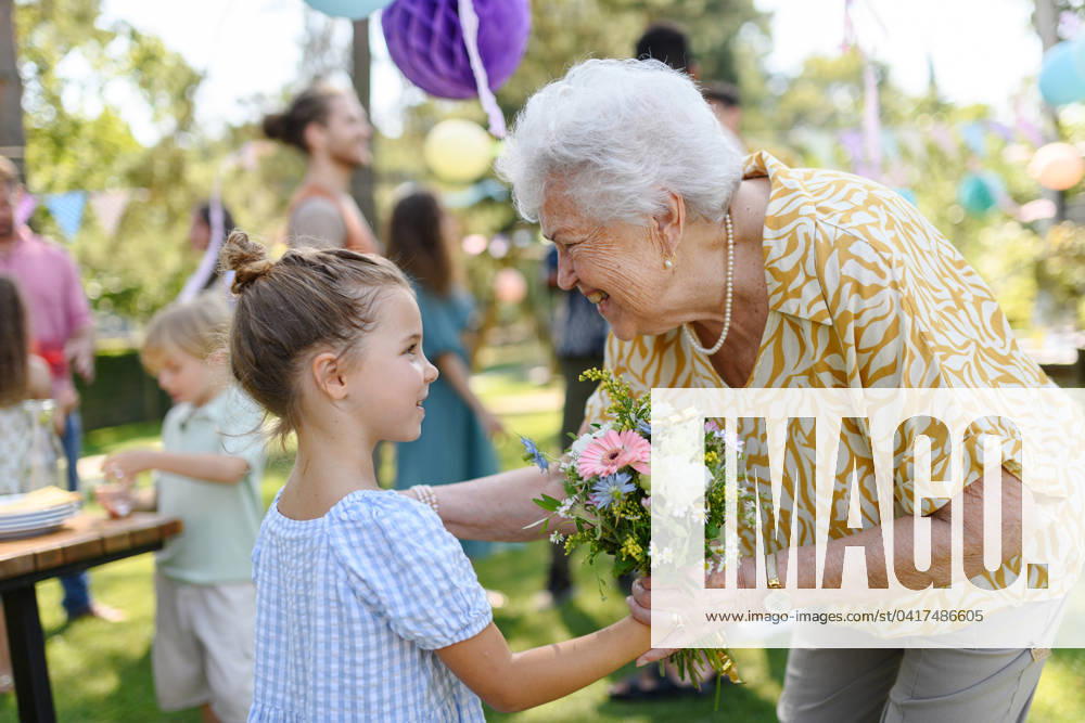 Garden birthday party for senior lady. Beautiful senior birthday woman receiving gift from granddaughter. Garden birthday party for senior lady. Beautiful senior birthday woman receiving gift from granddaughter, hugging. model released