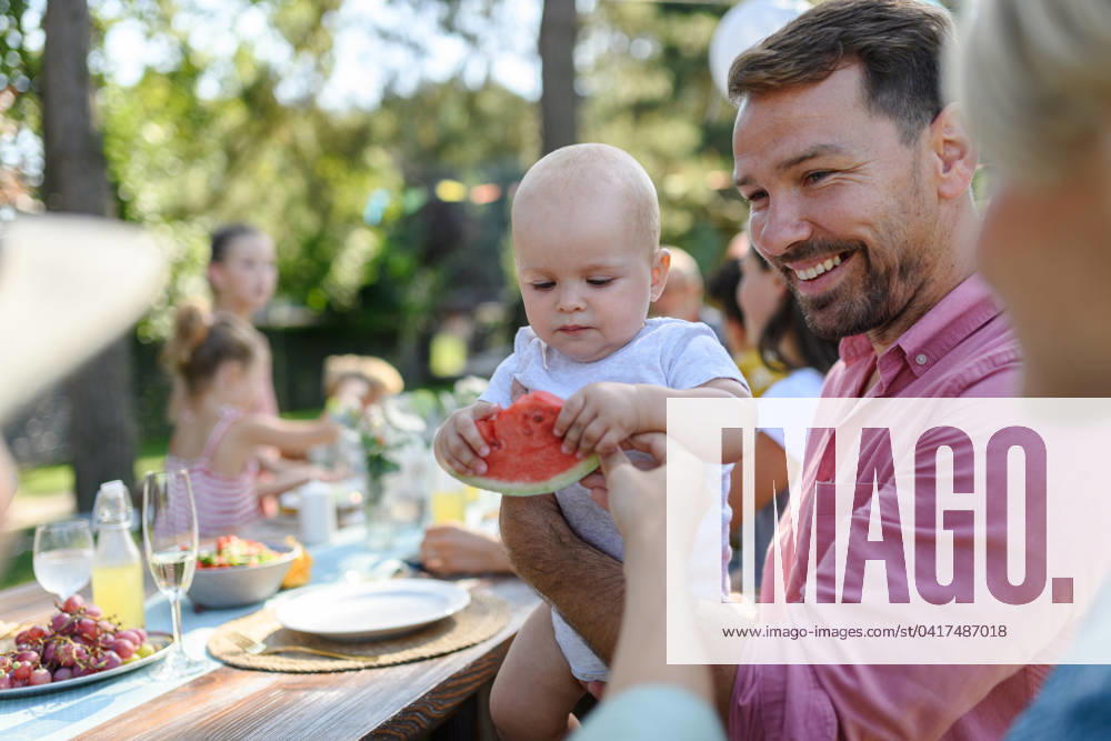 Cute baby eating watermelon at a summer garden party. Dad holding the baby boy in his arms and smiling. Cute baby eating watermelon at a summer garden party. Handsome father holding the baby boy in his arms and smiling. model released