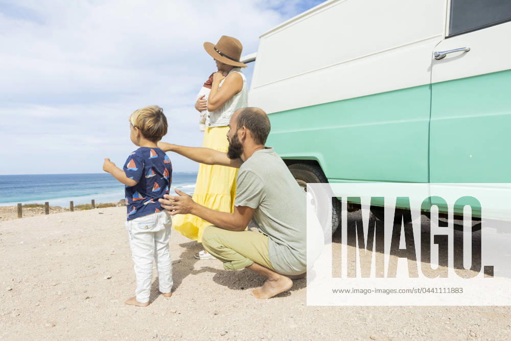 A young family enjoys a serene moment by the sea beside their retro van, embracing the joys of simple travel and togetherness. Model Released JuanAizpuru_ID19709_584473_016