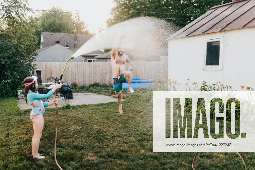 Young girl holds garden hose while dad runs through water Sioux Falls, South Dakota, United States CR_ASWE240317-1369124-01 ,model released, Symbolfoto ,property released