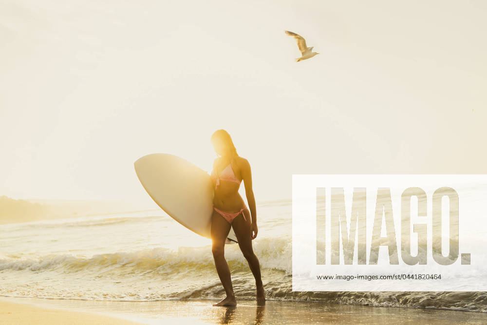 Young woman walking with surfboard near waves at sunset model released, Symbolfoto, AAZF01662