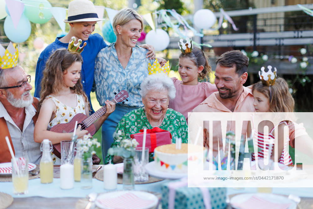 Garden birthday party for senior lady. Beautiful senior birthday woman receiving gift from family. Garden birthday party for senior lady. Beautiful senior birthday woman receiving gift from granddaughter, family and friends. Birthday celebration with paper crowns. model released