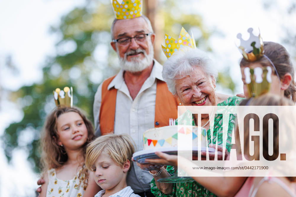 Garden birthday party for senior lady. Beautiful senior birthday woman receiving gift from family. Garden birthday party for senior lady. Beautiful senior birthday woman receiving gift from granddaughter, family and friends. Birthday celebration with paper crowns. model released
