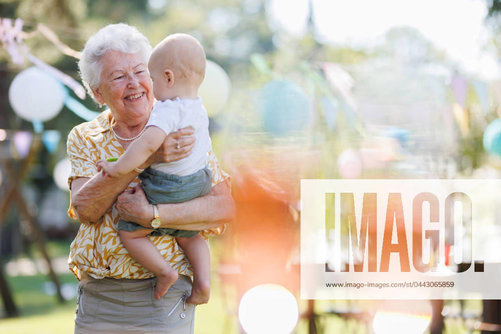 Great-grandmother holding little baby in her arms. Family summer garden party. Portrait of great-grandmother holding a tiny baby in her arms. Family summer garden party. model released