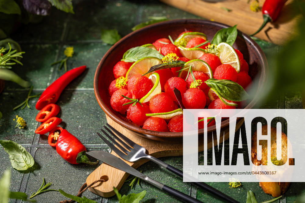 Spicy salad of fresh watermelon balls with basil, lime, rosemary and fennel, topping with olive oil Spicy salad of fresh watermelon balls with basil, lime, rosemary and fennel, topping with olive oil on dark green table surface with sunny light