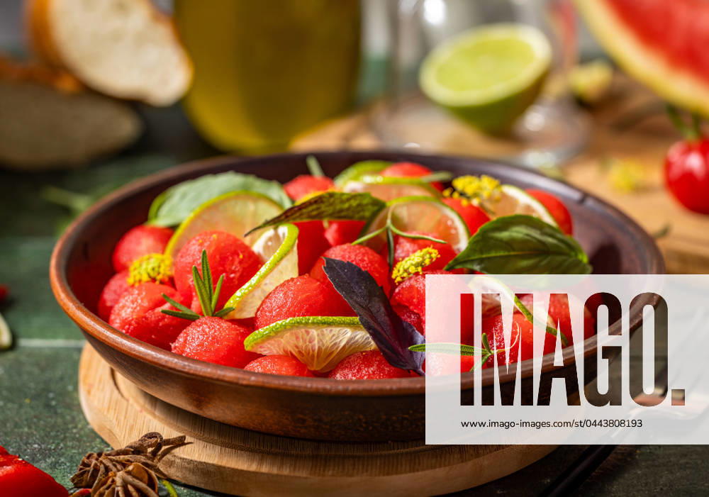 Spicy salad of fresh watermelon balls with basil, lime, rosemary and fennel, topping with olive oil Spicy salad of fresh watermelon balls with basil, lime, rosemary and fennel, topping with olive oil on dark green table surface with sunny light