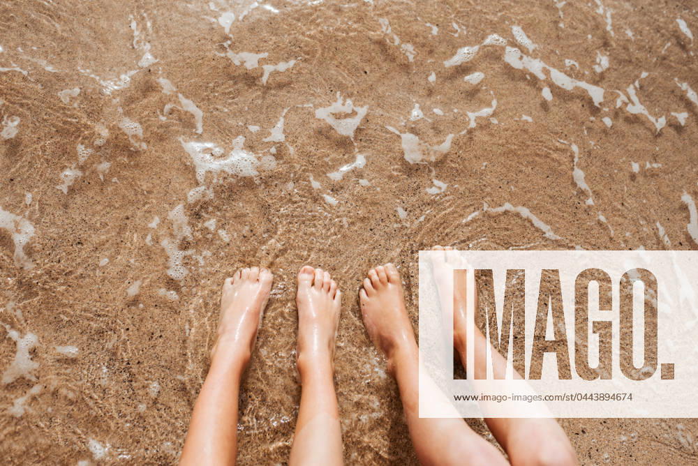 Close up of feet on beach with sea water beneath them. Sea foam and warm water soaking legs. Close up of feet on beach with sea water beneath. Sea foam and warm water soaking legs. model released
