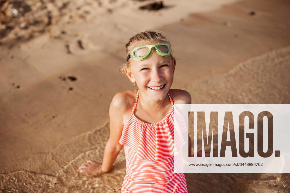 Young girl playing, swiming and splashing in fresh sea water. Smilling blonde girl in swimsuit with and swimming goggles. Concept of beach summer vacation with kids. Young girl on the beach. Smilling blonde girl enjoying sandy beach, looking at crystalline sea in Canary Islands. Concept of beach summer vacation with kids. model released