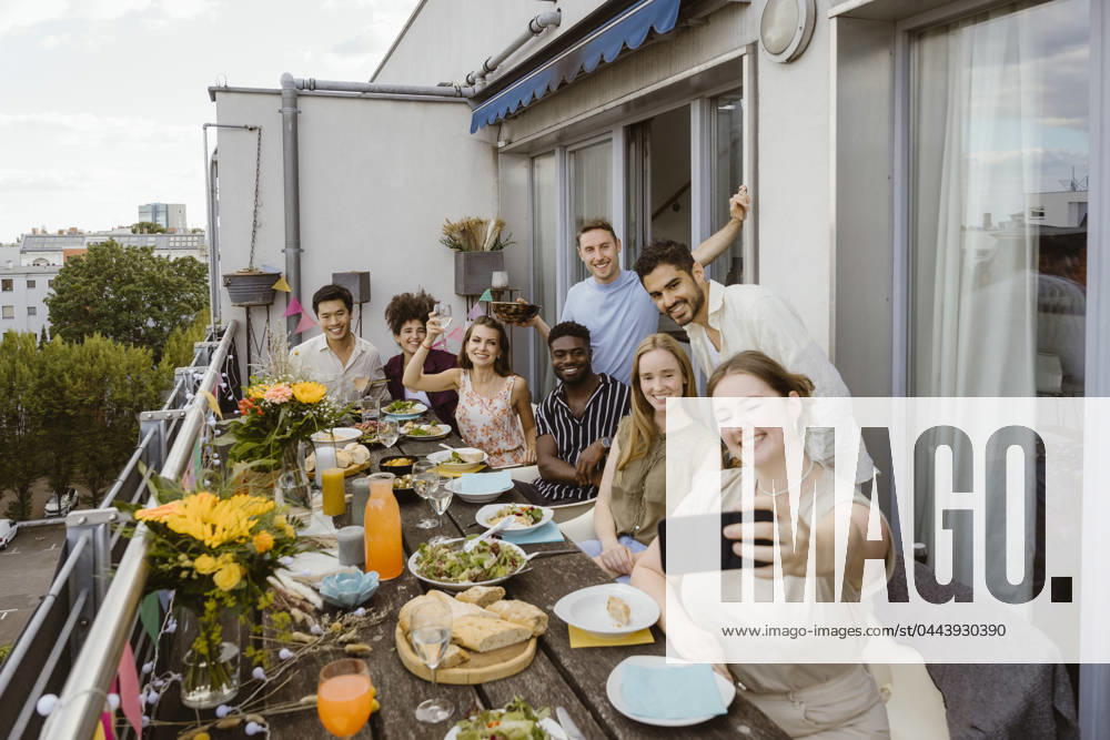 Smiling woman taking selfie with group of friends through smart phone while celebrating dinner party in balcony Germany, Berlin, model released, property released