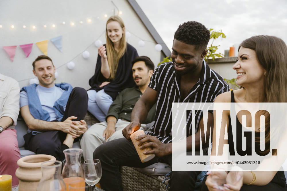 Smiling young man burning candle while sitting with male and female friends at party Germany, Berlin, model released, property released