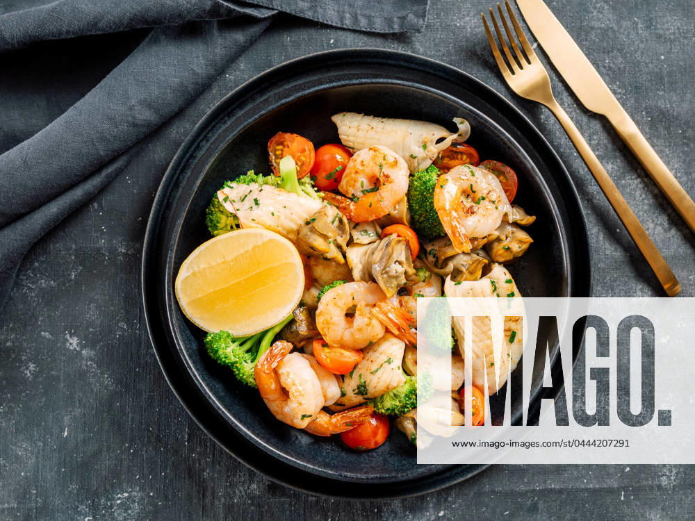 Salad with Mixed Seafood on dark plate Mixed Seafood Contain Shrimps, Mussels, Calamari Squids and Fish with Broccoli, Cherry Tomato, Lemon on Black dish in restaurant-style platting. Seafood salad on dark background. Top view