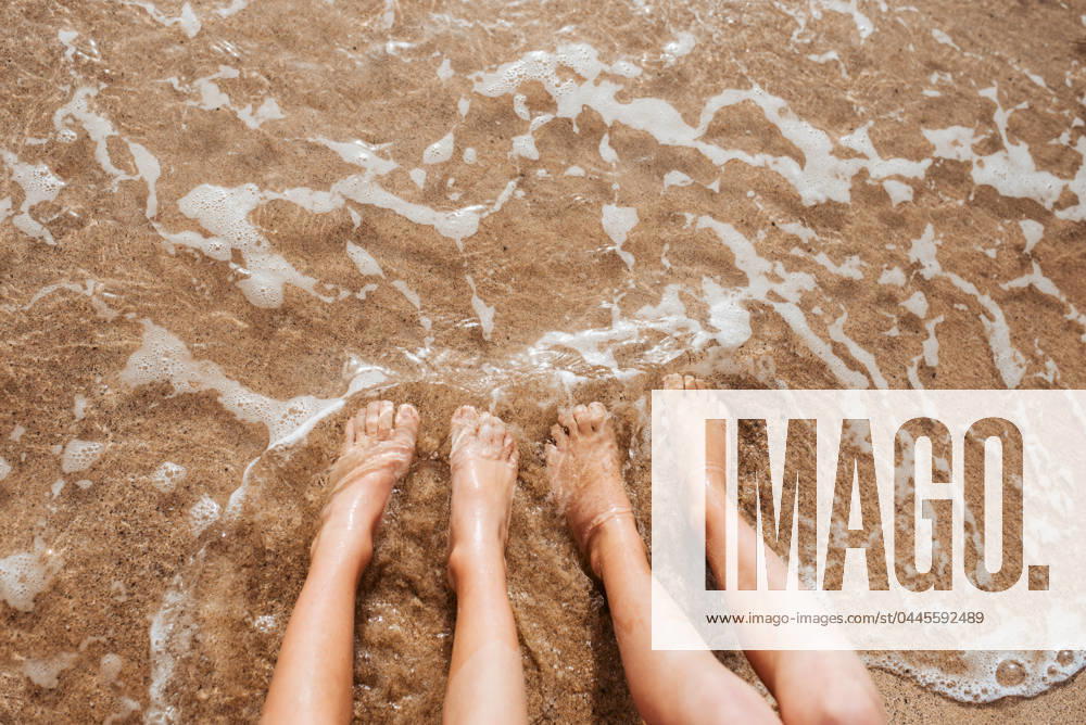 Close up of feet on beach with sea water beneath them. Sea foam and warm water soaking legs. Close up of feet on beach with sea water beneath. Sea foam and warm water soaking legs. model released