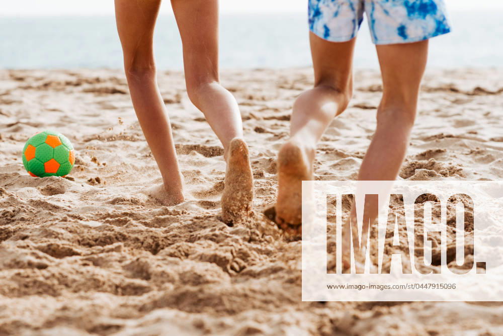 Siblings playing on beach with ball, playing football. Concept of family beach summer vacation with kids. Siblings playing on beach with ball, playing football. Concept of family beach summer vacation with kids. Close up on legs. model released