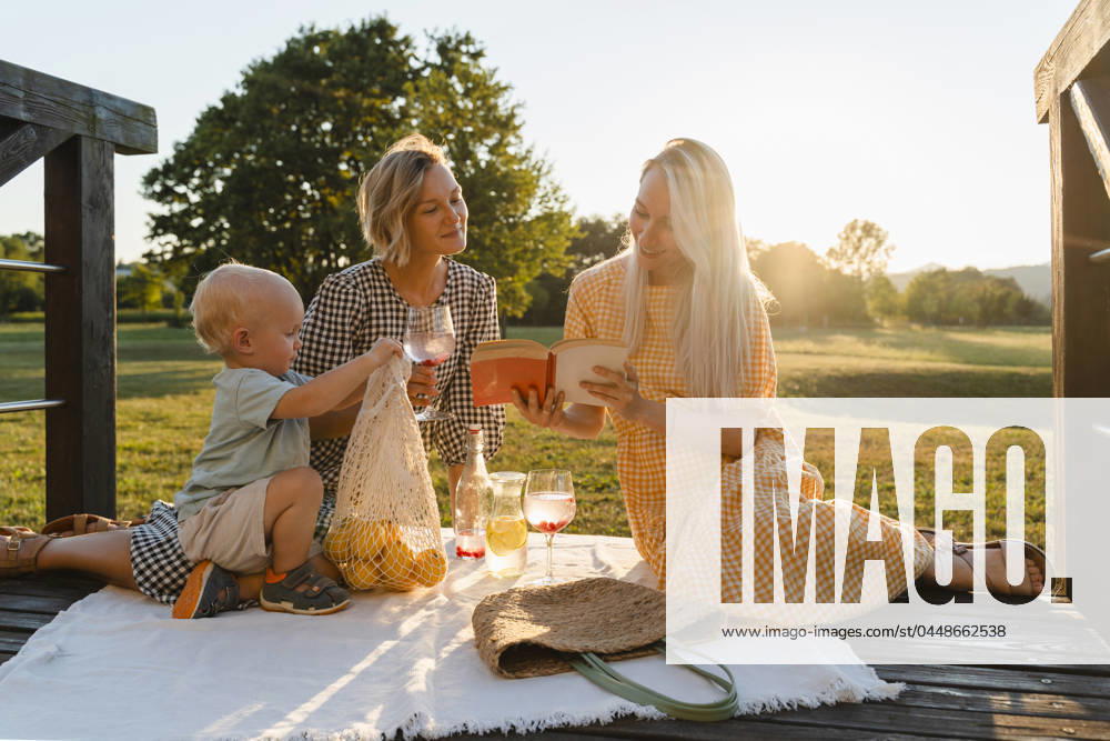 Women reading book sitting by toddler in park model released, Symbolfoto, NDEF01668