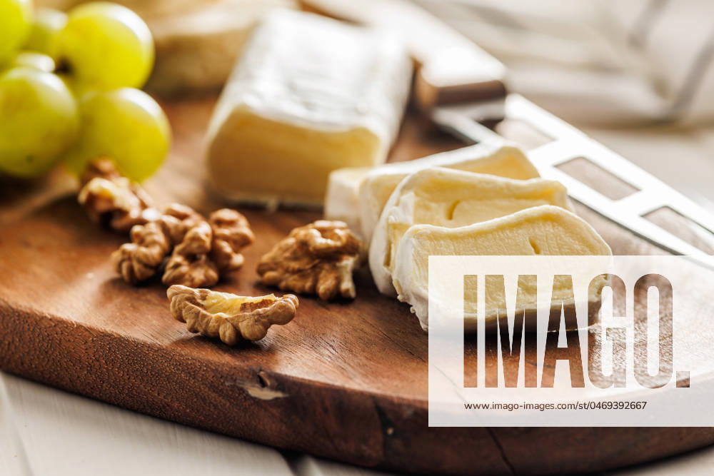Sliced Brie cheese on a wooden board Artisan Brie cheese sliced on a round wooden cutting board, served with grapes and walnuts, ideal image for Gourmet cheese concepts