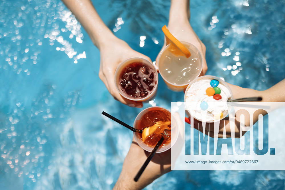 Close-up of female and male hands holding glasses with iced cocktails and clinking them. Friends make festive toast with delicious drinks against background of clear blue pool water. Close-up of female and male hands holding glasses with iced cocktails and clinking them. Friends make festive toast with delicious drinks against background of clear blue pool water. Party, vacation.