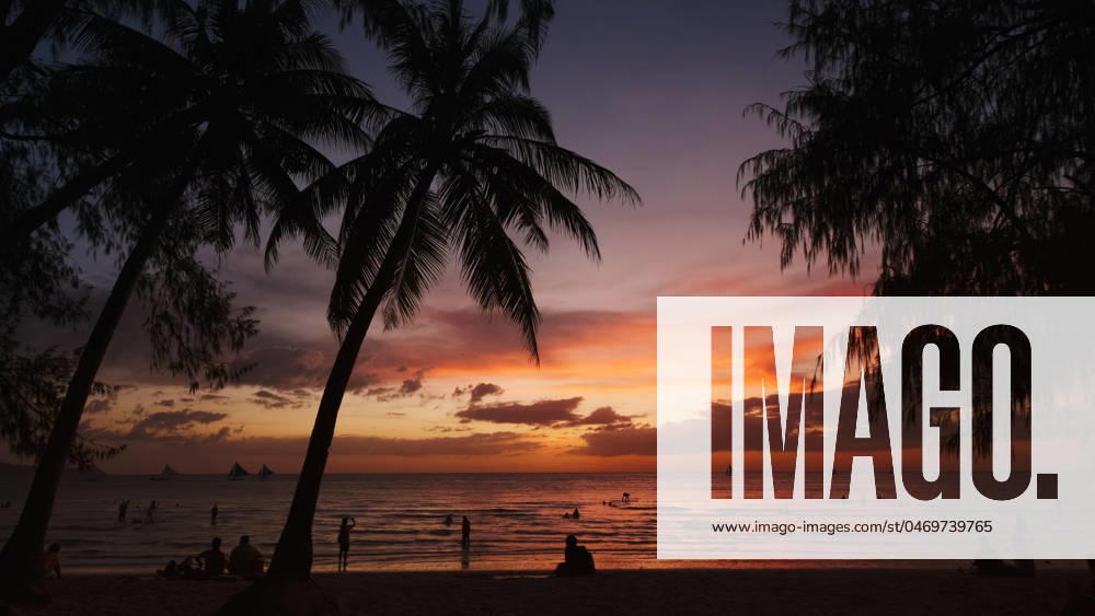 Sunset on beach with people and palms Silhouetted people and palms near sea. Sunset at tropical White beach, Boracay island, Philippines
