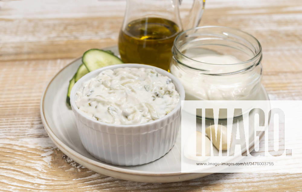 Traditional greek yogurt sauce Tzatziki,dressing in white bowl, made of grated cucumbers, sour cream yogurt,olive oil,garlic,herbs with ingredients on wooden table. Close up, horizontal Traditional greek yogurt sauce Tzatziki in white bowl, made of chopped cucumbers, sour cream yogurt,olive oil,garlic,herbs with ingredients on wooden table. Rustic style. Close up, horizontal plane.