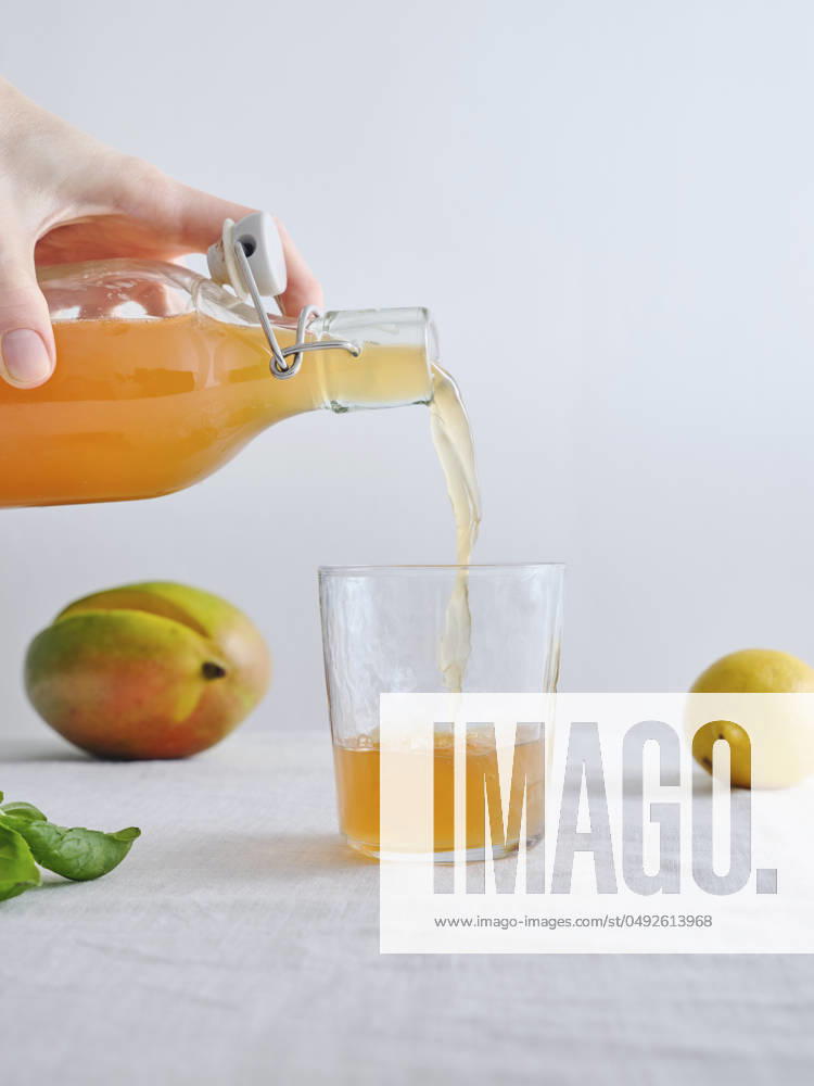 Female hand pouring organic homemade fermented kombucha from a bottle into a glass Female hand pouring organic homemade fermented kombucha lemonade from a bottle into a glass