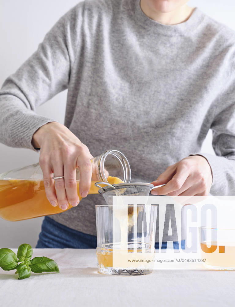Female model pouring organic homemade komucha from a bottle into a glass Female model pouring organic homemade komucha from a bottle into a glass standing on white background