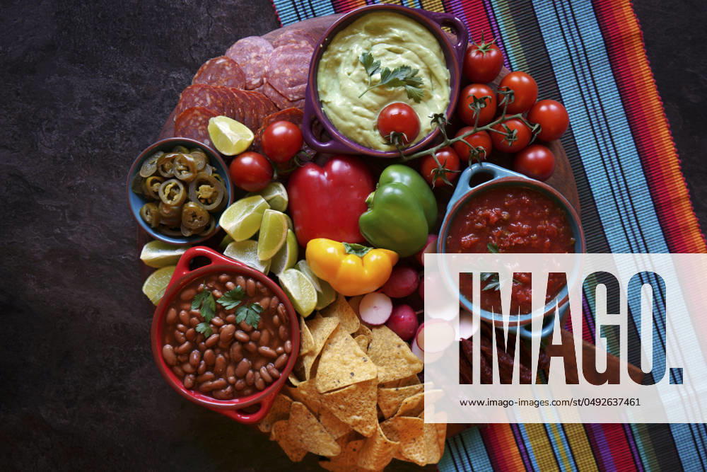 Mexican theme charcuterie board grazing platter with guacamole, salsa, beans, jalapenos, chorizo, and tortilla chips. Mexican theme charcuterie board grazing platter with guacamole, salsa, beans, jalapenos, chorizo, and tortilla chips.