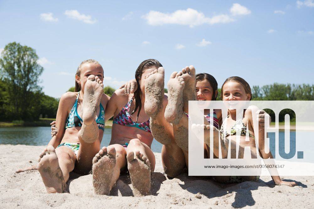 Freundinnen sitzen am Strand und strecken die sandigen Füße in die Kamera