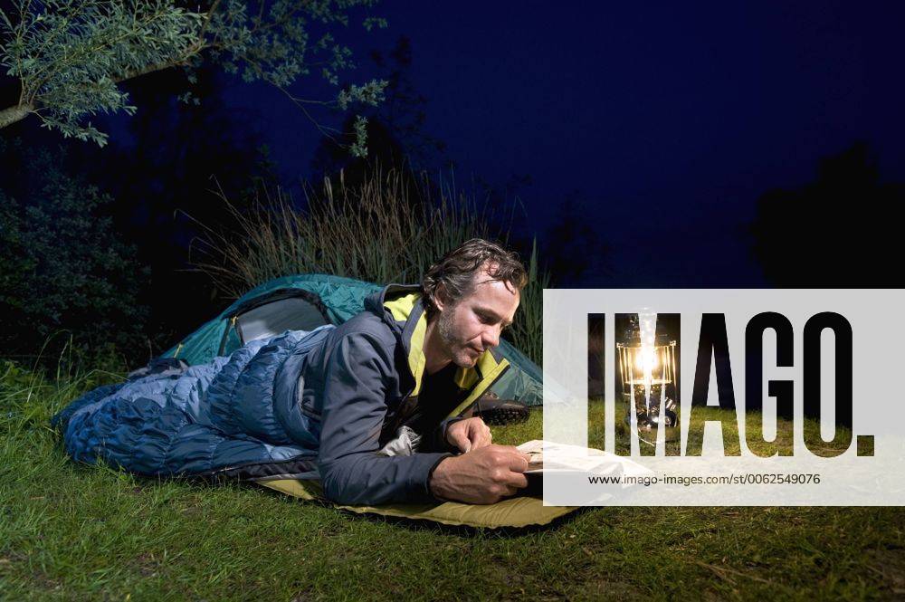 Germany, Bavaria, Ammersee, Man reading book near lakeshore while camping at night model released RNF000615
