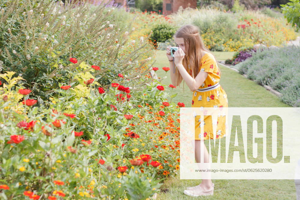IMAGO Creative: Sommer, Sommertage im Stadtpark Girl in yellow dress photographing flowers in a vibrant garden. Oklahoma City, Oklahoma, United States R_KSRA240623D-1452781-01 ,model released, Symbolfoto