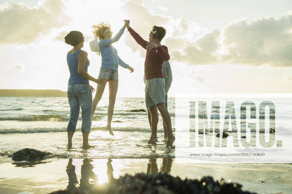 IMAGO Creative, Jahreszeit Sommer, Sommerferien Woman and three teenagers having fun on the beach by sunset model released Symbolfoto UUF001716