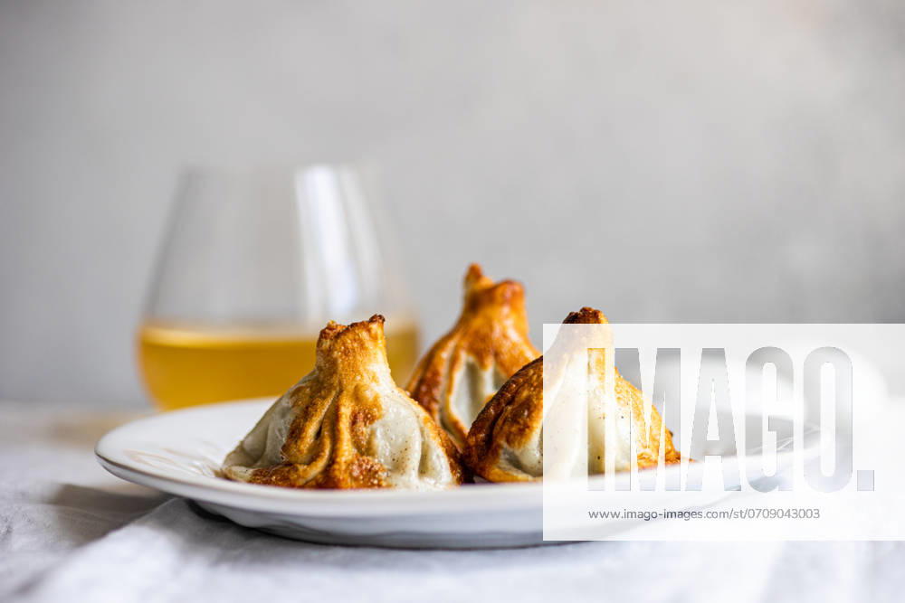 IMAGO Creative, Food, Dumplings Authentic Georgian khinkali dumplings served on a white plate, expertly cooked A clear glass of white wine complements the scene, heightening the culinary appeal Model Released AnnaBogush_ID22388_654127_006