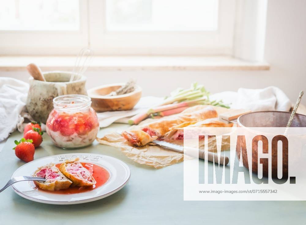 Delicious strawberry rhubarb strudel cake on sunny kitchen table with ingredients at window. Homemade seasonal cuisine ,model released, Symbolfoto