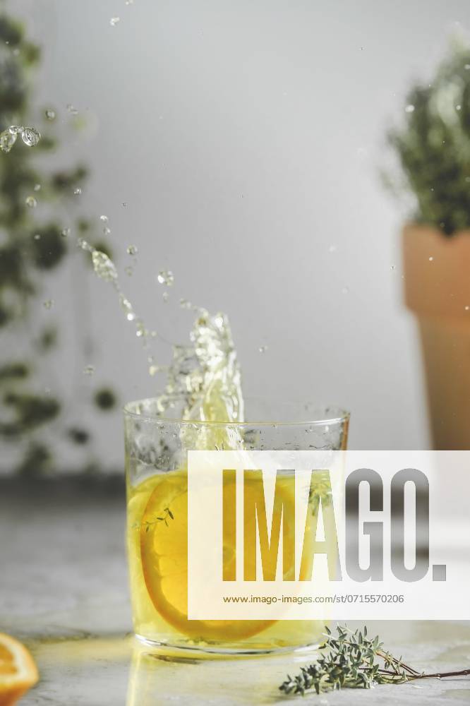 Homemade splashing orange lemonade in glass with thyme on kitchen table at wall and plant background. Refreshing drink with summer fruit. Front view. ,model released, Symbolfoto