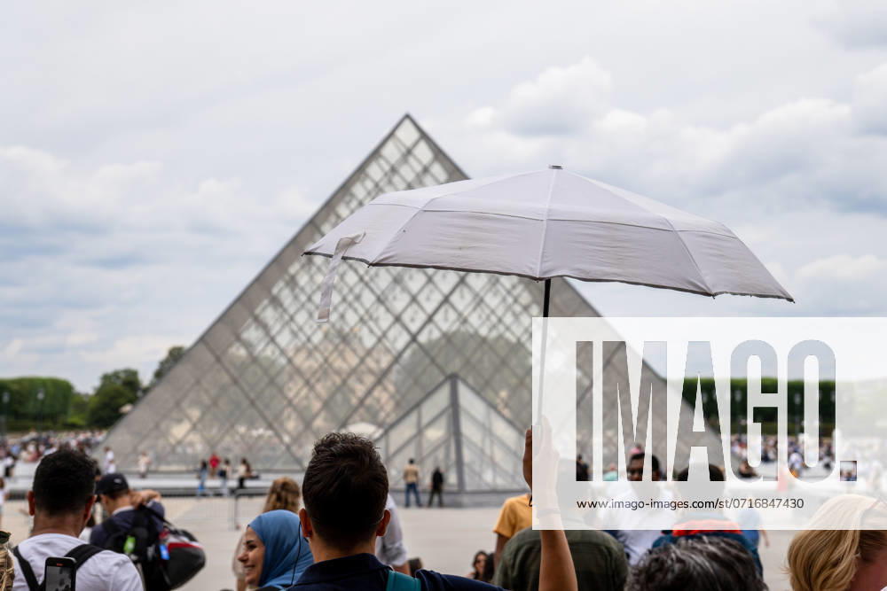In front of the Louvre Museum in Paris, tourists protect themselves from the summer heat with a parasol while queuing in front of the famous glass pyramid