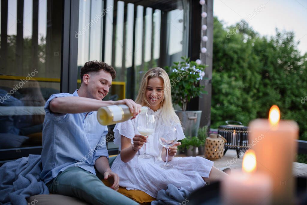 A young couple clinking with wine outdoors, weekend away in tiny house in countryside, sustainable living.