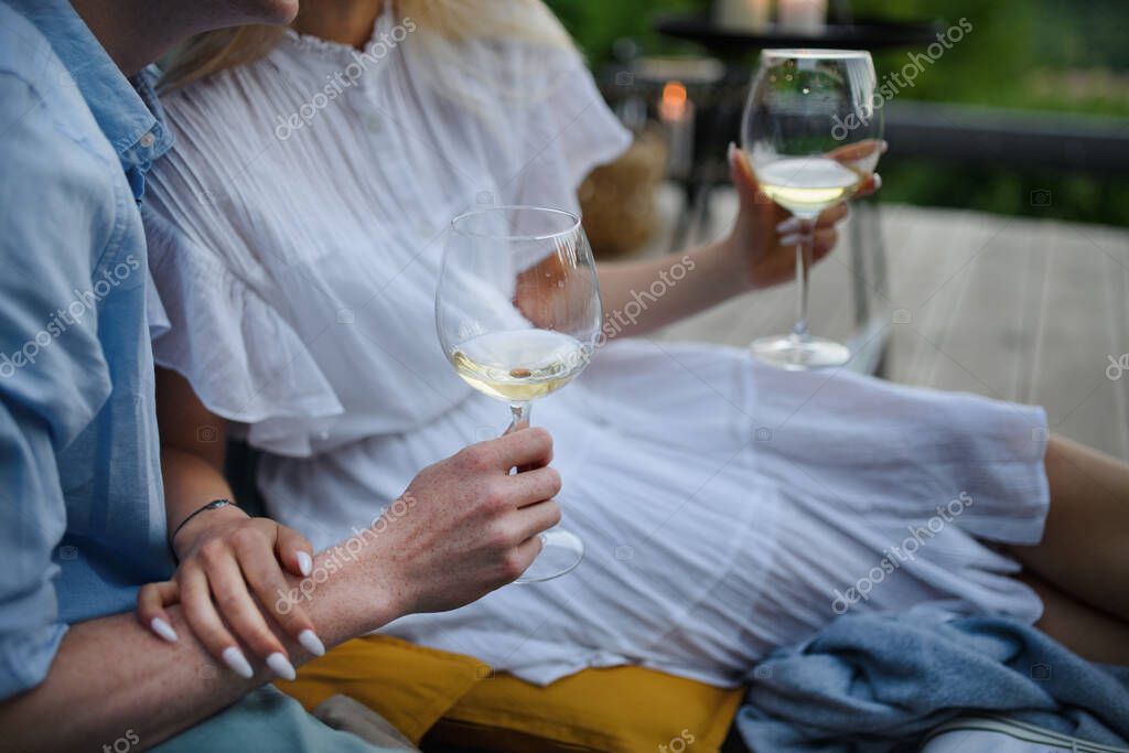 A young couple clinking with wine outdoors, weekend away in tiny house in countryside, sustainable living. Close-up.