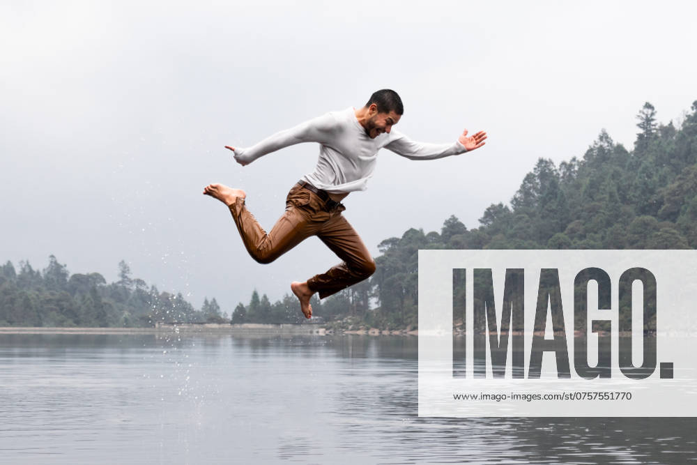 A man performs an energetic jump over a serene lake on a misty, rainy day, surrounded by tranquil forest and gentle raindrops, creating a sense of freedom and exhilaration Model Released EduardoGavira_ID23395_679858_011