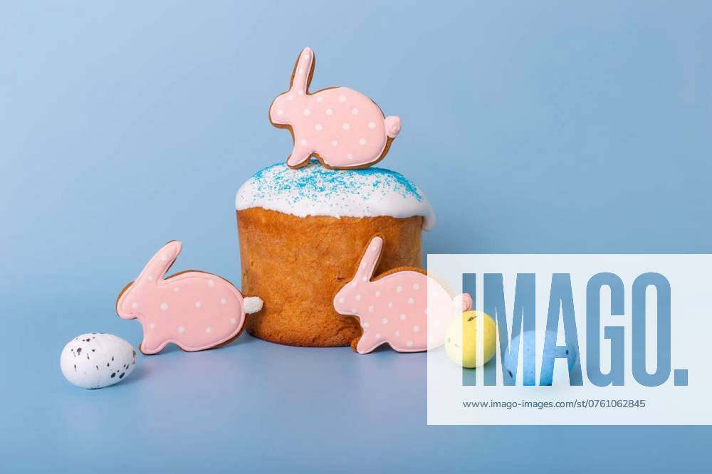 Three cute pink gingerbreads in the form of a rabbit on Easter cake, Three cute pink gingerbreads in the form of a rabbit on Easter cake stand on a blue background., Three cute pink gingerbreads in the form of a rabbit on Easter cake stand on a blue background., 04.08.2024,