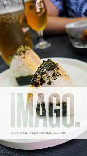 IMAGO Creative, Food, Japan, Onigiri Close-up of two onigiri rice balls with seaweed and seasoning on a white plate, with beverages in the background. 25793096 RECORD DATE NOT STATED