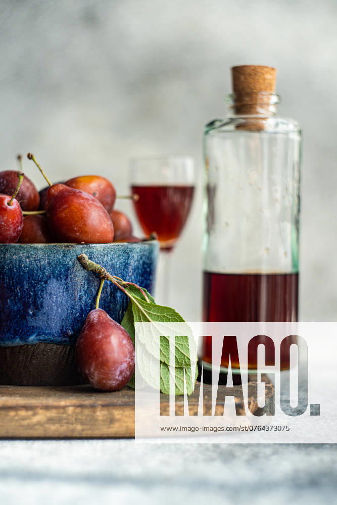 IMAGO Creative, Jahreszeit Sommer, Food, Pflaume A bowl of fresh, organic plums alongside a bottle of homemade plum liqueur, captured from the side. The image highlights ripe plums with vibrant colors and a glass of plum liqueur, suggesting a cozy, autumnal setting. Model Released AnnaBogush_ID23878_692882_013