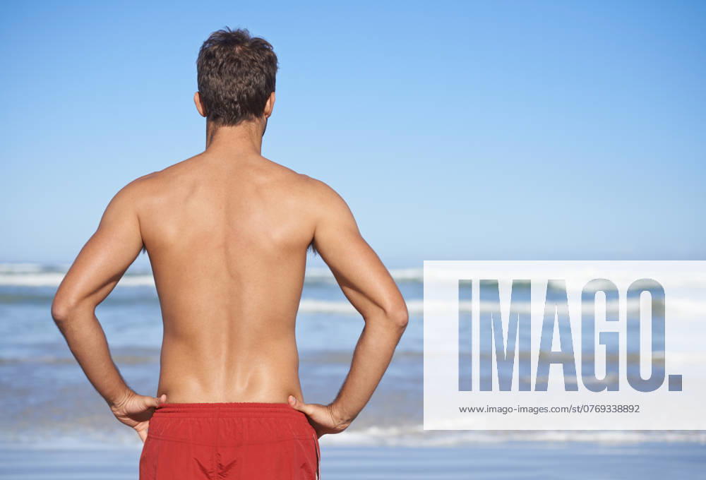 Man, lifeguard and beach for security, emergency or outdoor swimming in health and safety. Rear view or back of male person or professional swimmer stranding ready for patrol at sea or ocean coast. model released property released