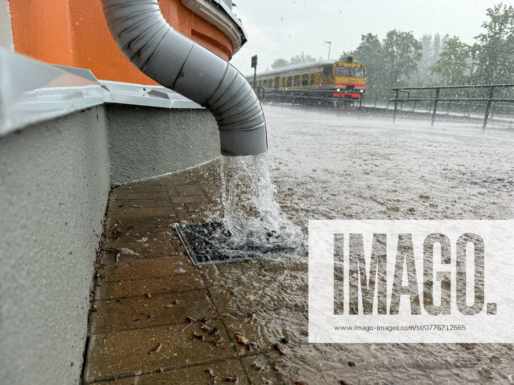 Gutter by the wall of the building and train in the background, rapid flow of water after heavy rain.
