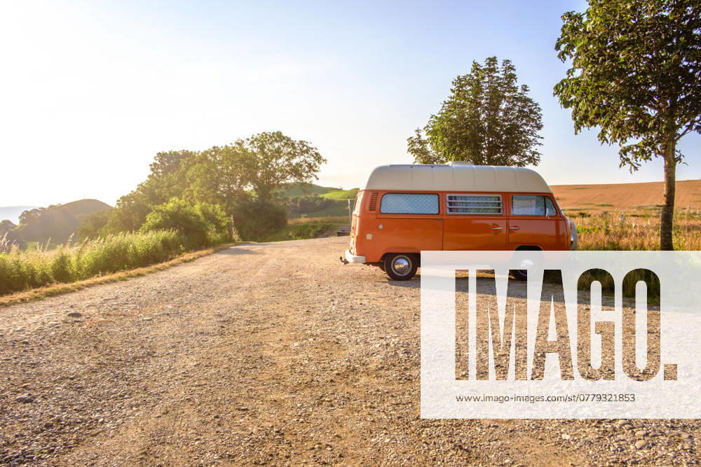 An orange and white VW Bus van stands on a gravel parking lot on a summer morning, Baden Württemberg, Germany A van stands in the landscape