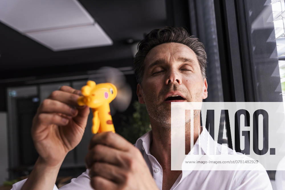 IMAGO Creative, Jahreszeit Sommer, Hitze Businessman using hand fan on face in office model released, Symbolfoto property released, UUF33640