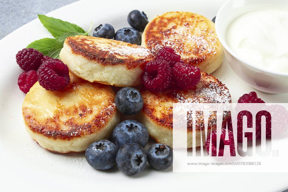 Frühstück, Hüttenkäsekuchen, mit frischen Beeren und saurer Sahne, Draufsicht, Nahaufnahme, ohne Personen Breakfast, cottage cheese cakes, with fresh berries, and sour cream, top view, close-up, no people