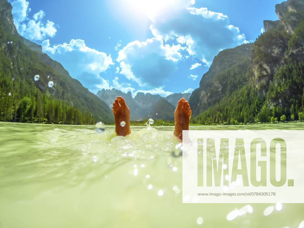 Füße eines Touristen, der im türkisfarbenen Wasser des Lago di Landro schwimmt, umgeben von dem atemberaubenden Panorama der Dolomiten an einem sonnigen Sommertag Feet of a tourist floating in the turquoise water of lago di landro, surrounded by the breathtaking panorama of the dolomites on a sunny summer day