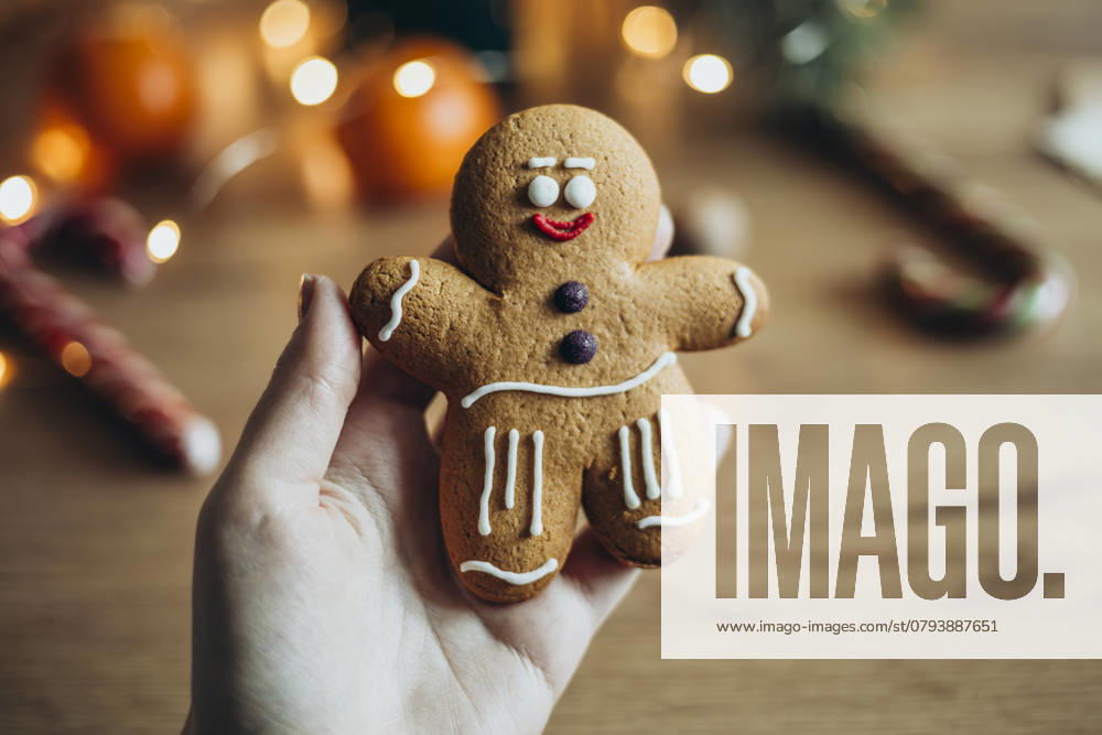 IMAGO Creative, Weihnachten, Food, Backen, Lebkuchen A hand holds a charming gingerbread man cookie decorated with icing Soft lighting and blurred holiday decor create a warm, festive ambiance Ideal for holiday themes Model Released HannaYakimenko_ID25894_748059_019