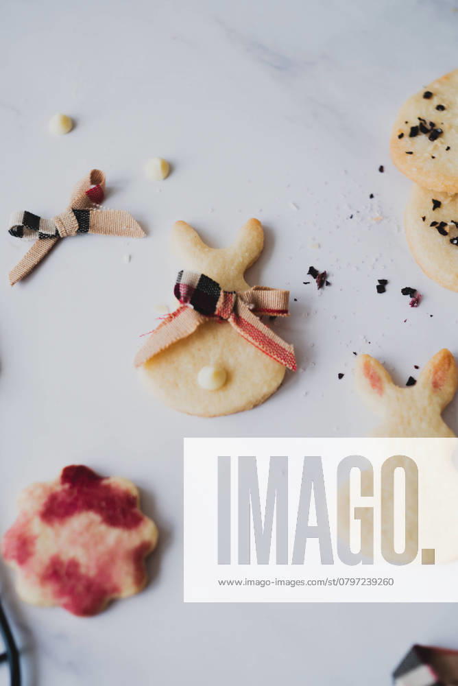 Top view of homemade Easter bunny cookies intricately decorated with hibiscus tea for a natural red hue, scattered across a marble surface. Model Released CamilaMacedo_ID26013_750672_001