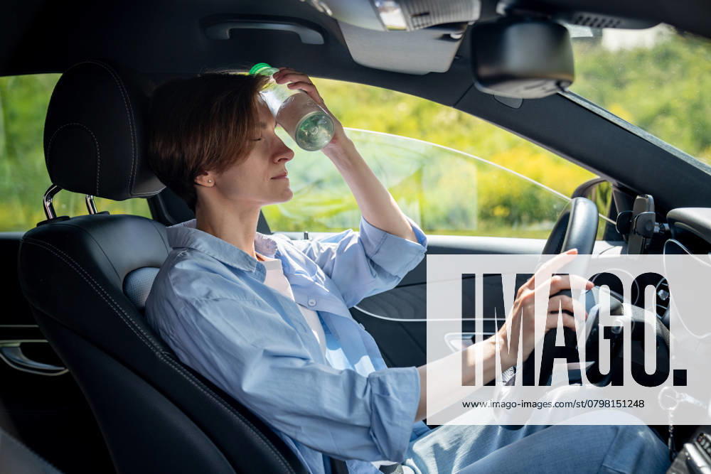 IMAGO Creative, Jahreszeit Sommer, Hitze Vor Hitze erschöpfte Frau sitzt im Auto und hält sich mit geschlossenen Augen eine kalte Flasche an die Stirn Hot weather for drivers. Tired from heat woman in car cooling forehead with cold bottle of water. Exhausted female take break in car park suffering from heat in summer city feeling dizziness pressure ,model released, Symbolfoto