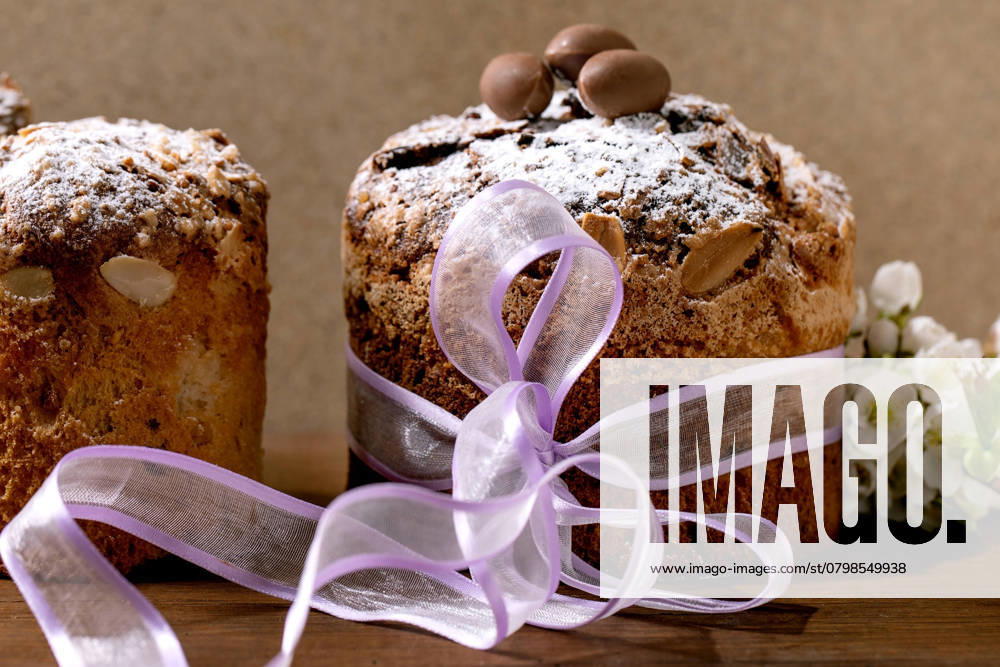 Traditioneller italienischer Oster-Panettone-Kuchen Homemade Italian traditional Easter panettone cake, decorated by chocolate eggs, pink ribbon and blossoming cherry tree flowers standing on wooden table. Traditional Easter European bake. Close up