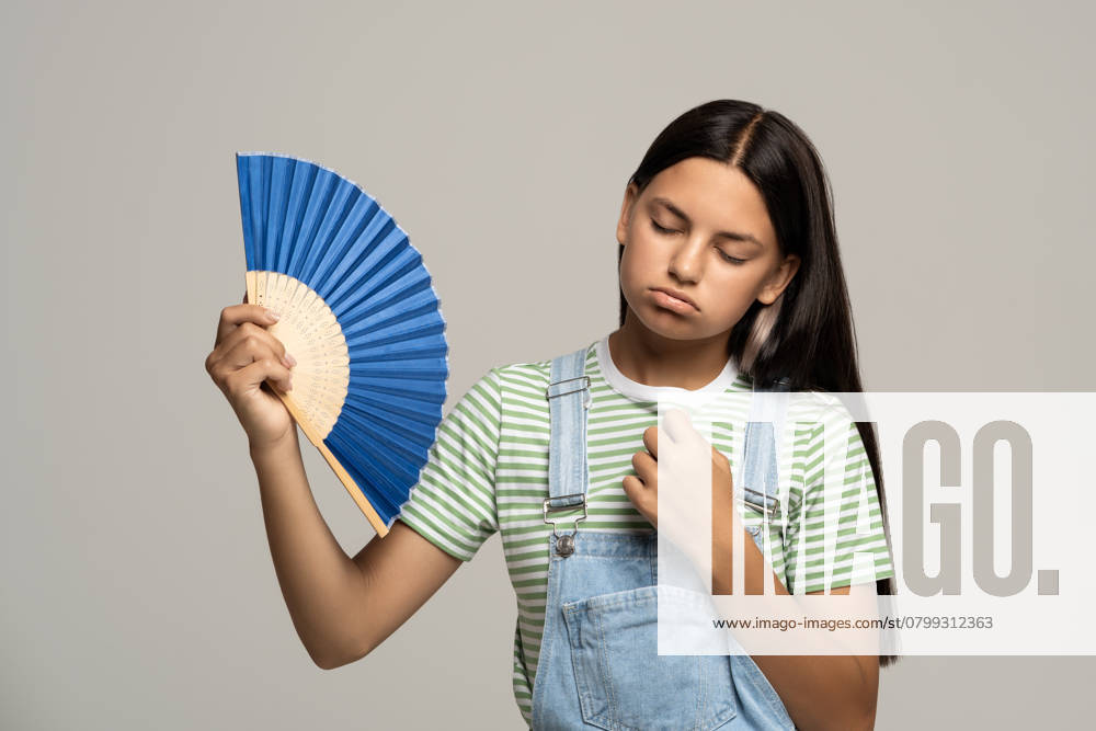 IMAGO Creative, Jahreszeit Sommer, Hitze Verschwitztes, erschöpftes Teenager-Mädchen, das einen Papierfächer benutzt, leidet unter der Hitze. Überhitzung, Verstopfung, heißes Wetter Verschwitztes, erschöpftes Teenager-Mädchen, das einen Papierfächer benutzt, leidet unter der Hitze. Überhitzung, Verstopfung, heißes Wetter ,model released, Symbolfoto